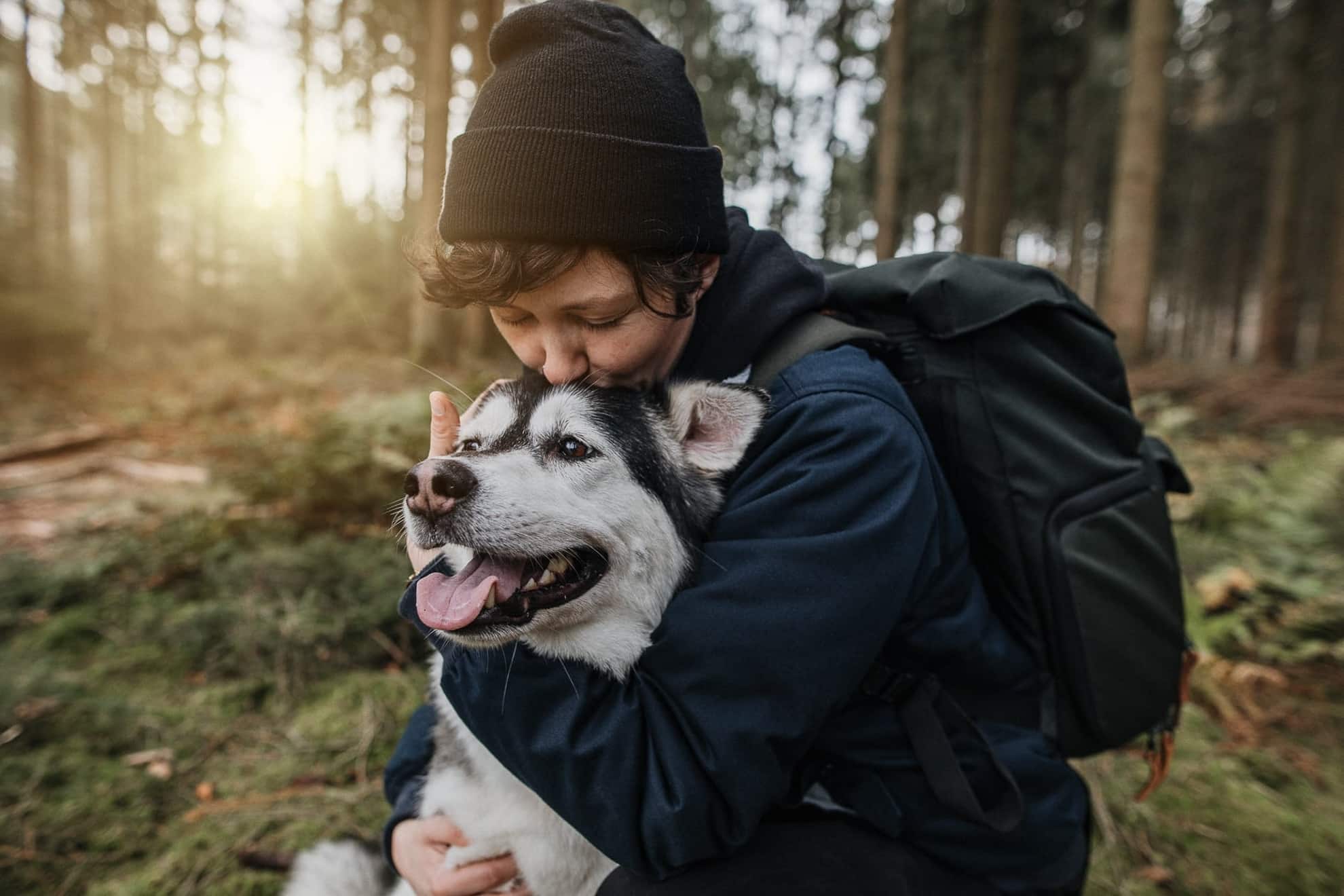 Junger Mann umarmt seinen Hund innig im Wald bei Sonnenuntergang