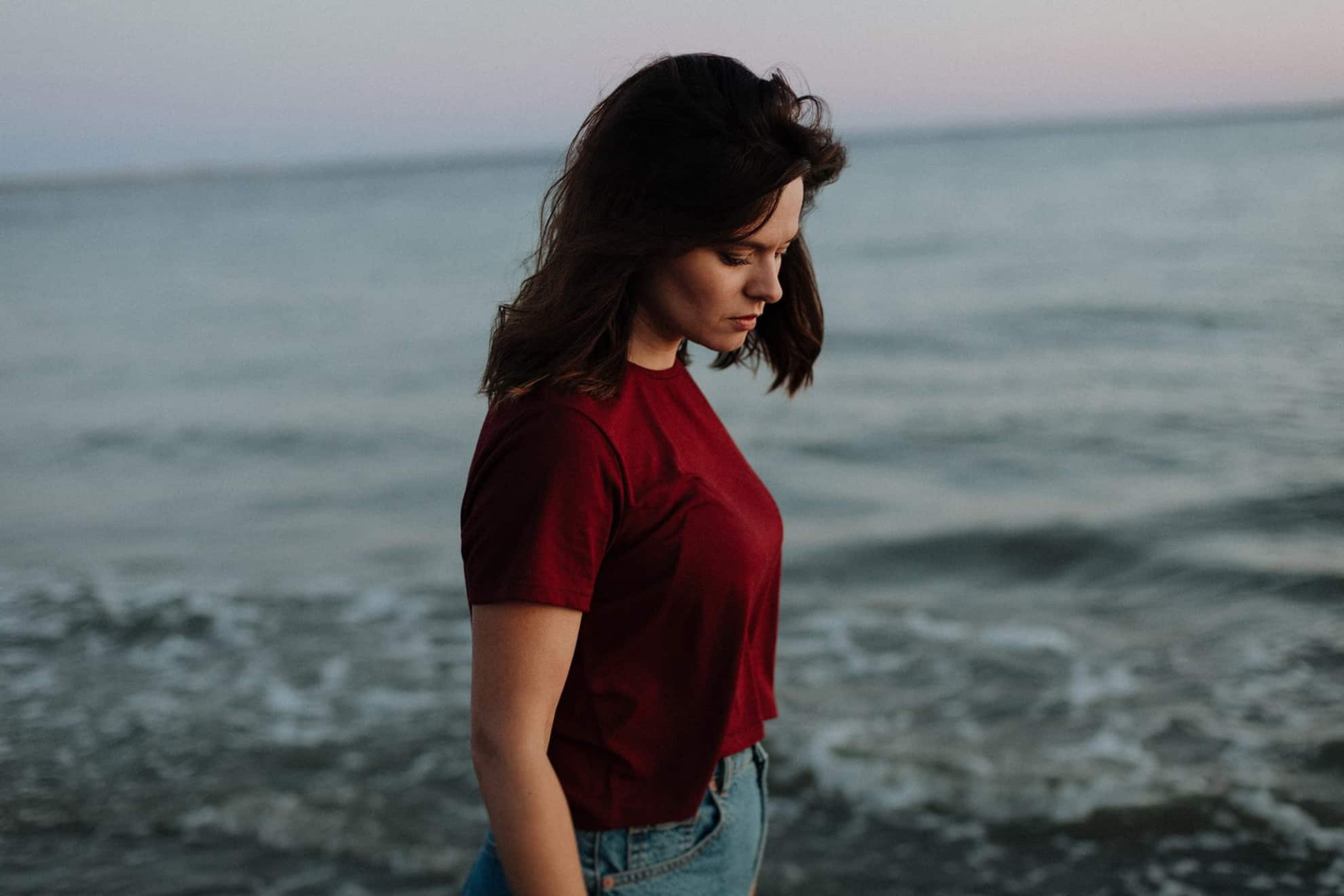 Junge Frau im roten T-Shirt am Meer bei Sonnenuntergang
