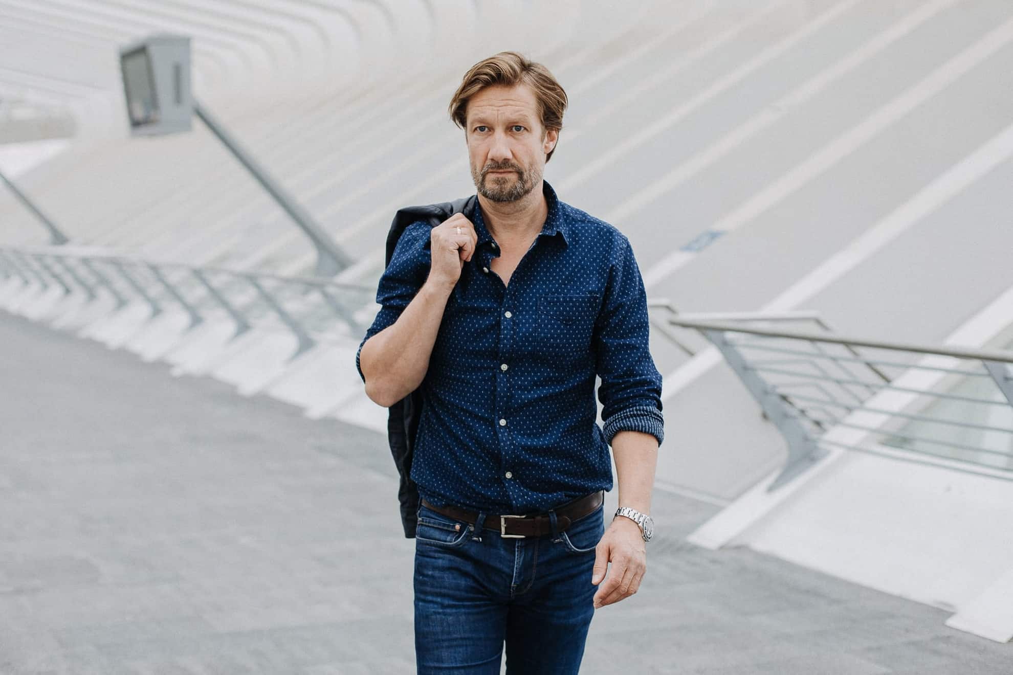 Christoph Kottenkamp spaziert vor modernem hellen Hintergrund in blauem Hemd und blauer Jeans
