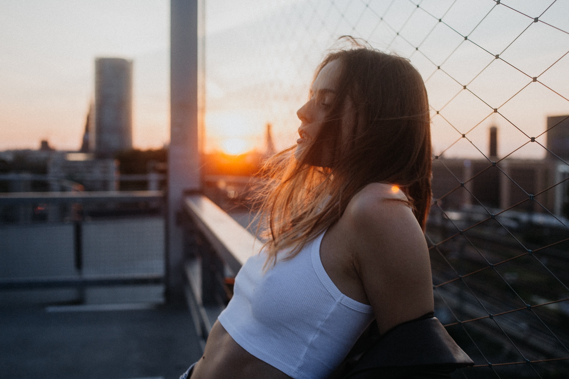 Junge attraktive Frau im auf einem Parkdeck an ein Netz angelehnt bei Sonnenuntergang